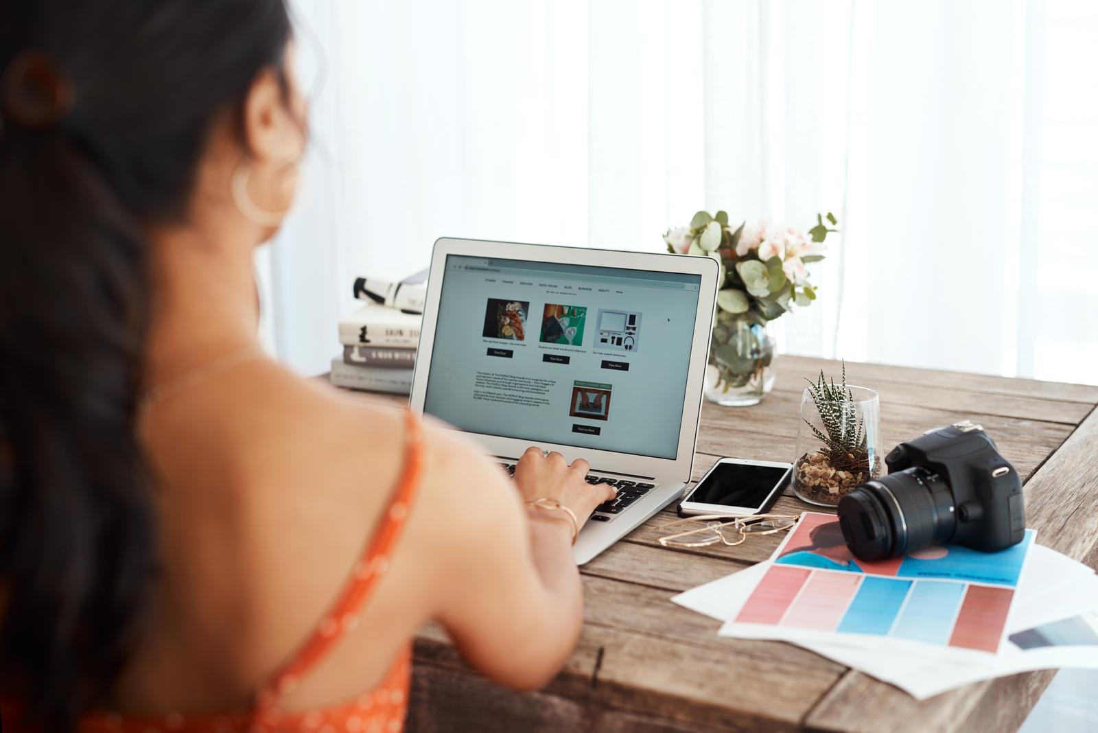 A woman sitting at a table with a laptop and a camera.